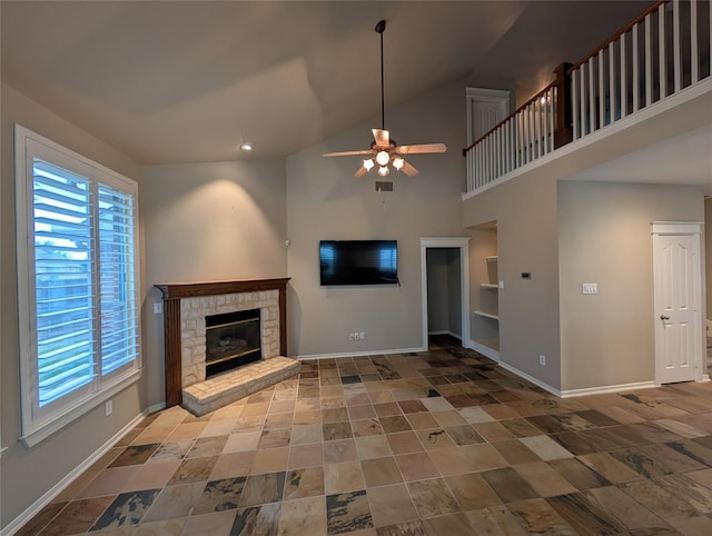 unfurnished living room featuring stone finish flooring, ceiling fan, a stone fireplace, and baseboards