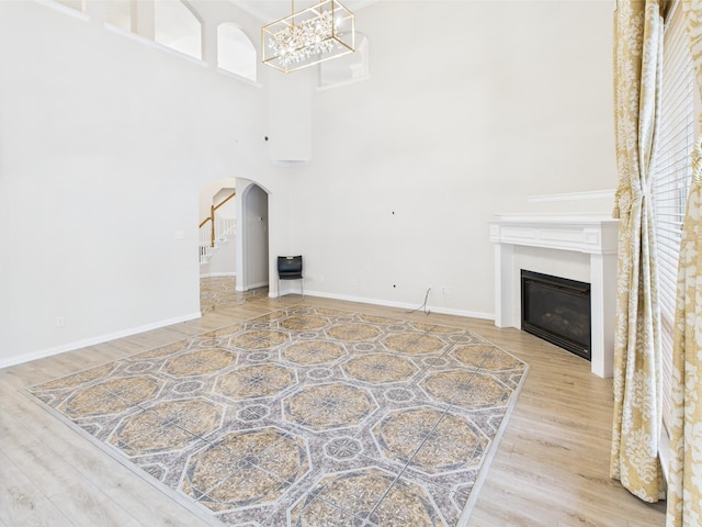1264 Carriage Creek Dr, Desoto, TX 75115 - unfurnished living room featuring arched walkways, a chandelier, wood finished floors, a high ceiling, and a glass covered fireplace