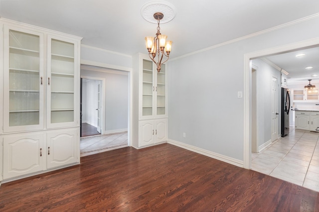 unfurnished dining area with an inviting chandelier, baseboards, crown molding, and wood finished floors