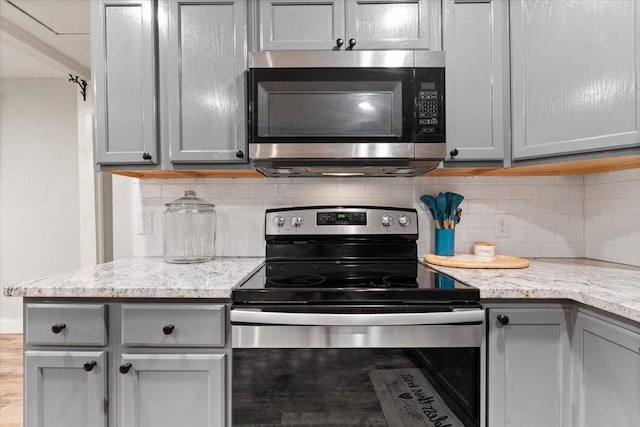 kitchen with gray cabinetry, light stone counters, appliances with stainless steel finishes, and tasteful backsplash