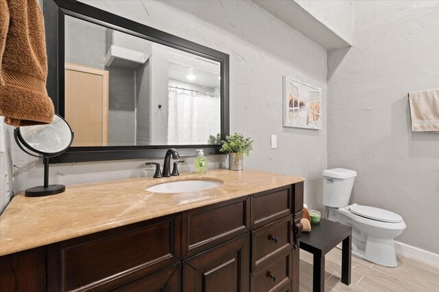 full bathroom with baseboards, wood finished floors, toilet, and vanity