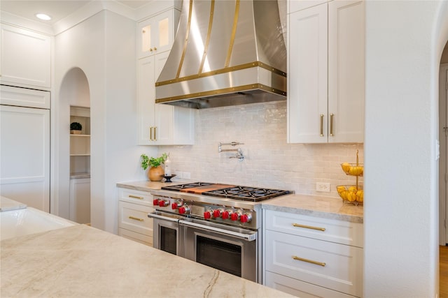 5409 Twin Cities Ln, Mckinney, TX 75070 - kitchen with wall chimney exhaust hood, range with two ovens, arched walkways, and white cabinets