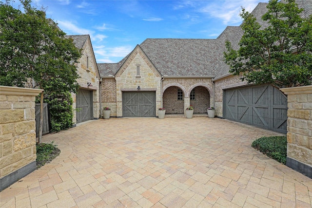 5409 Twin Cities Ln, Mckinney, TX 75070 - french country style house featuring stone siding, an attached garage, driveway, roof with shingles, and brick siding