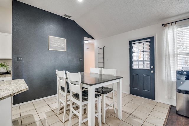 dining space with visible vents, light tile patterned flooring, and vaulted ceiling