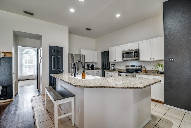 kitchen with visible vents, a sink, a kitchen island with sink, and stainless steel appliances
