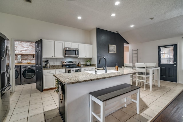 kitchen with a sink, a textured ceiling, stainless steel appliances, lofted ceiling, and washer and clothes dryer