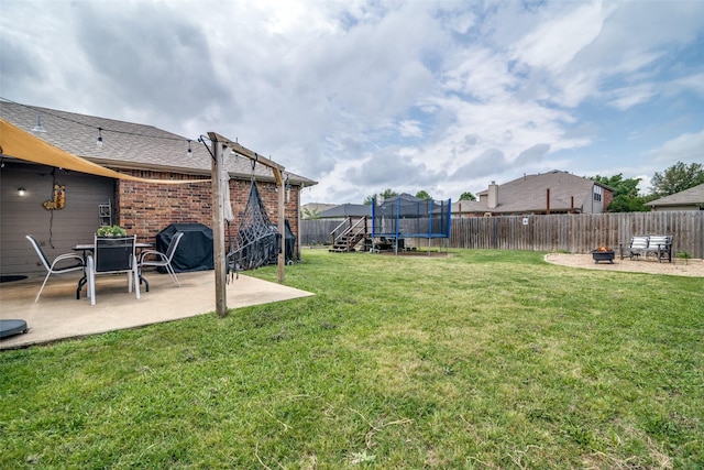 view of yard featuring a patio, a fenced backyard, a trampoline, and a fire pit