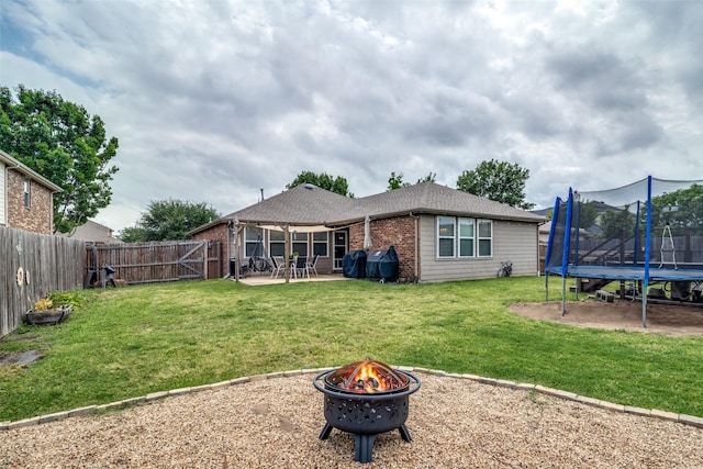 rear view of house featuring a fenced backyard, a patio area, a lawn, a trampoline, and an outdoor fire pit