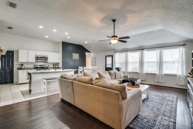 living room featuring ceiling fan, light wood-style floors, a textured ceiling, lofted ceiling, and visible vents