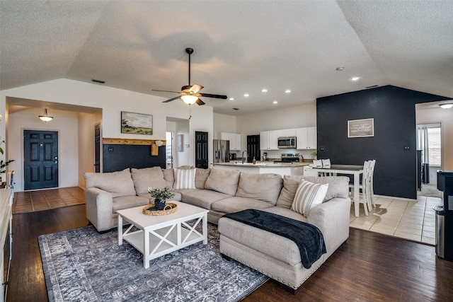 living area featuring a ceiling fan, a textured ceiling, vaulted ceiling, and light wood finished floors