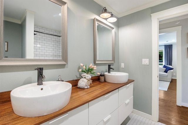 ensuite bathroom featuring crown molding, double vanity, a sink, and wood finished floors