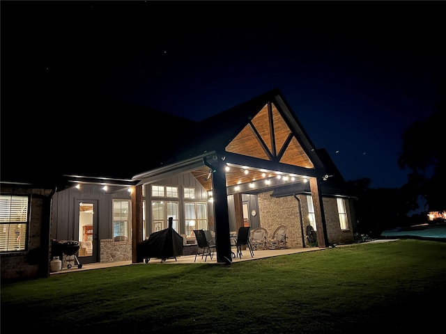 back of house at twilight featuring a lawn and a patio area