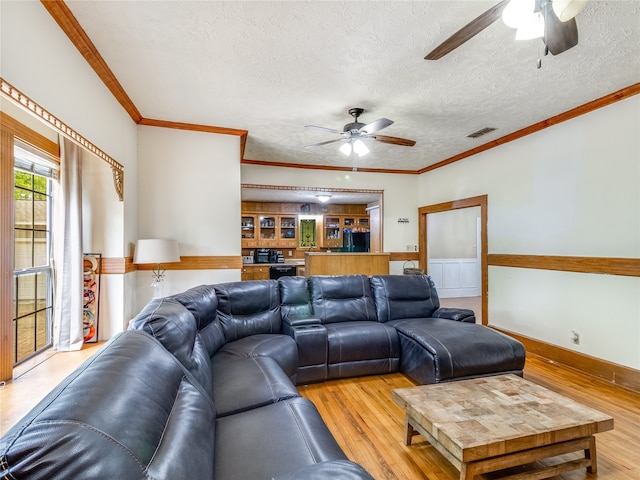 living area with a ceiling fan, a textured ceiling, visible vents, light wood-style floors, and ornamental molding