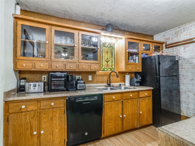 kitchen featuring brown cabinetry, light countertops, a sink, light wood-style flooring, and black appliances