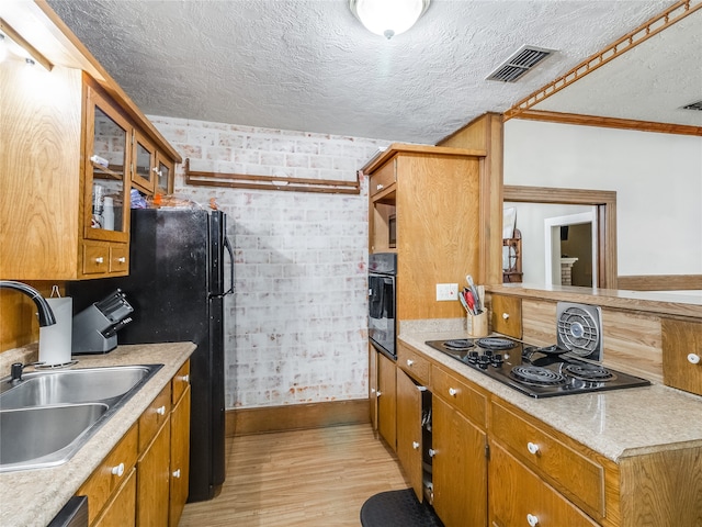 kitchen featuring a sink, light wood finished floors, light countertops, visible vents, and black appliances