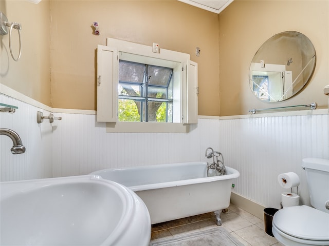 bathroom featuring toilet, a freestanding tub, tile patterned flooring, and a wainscoted wall