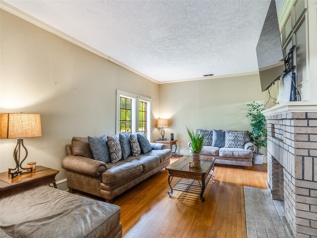 living room featuring crown molding, a textured ceiling, a brick fireplace, and hardwood / wood-style flooring