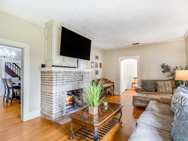 living room featuring visible vents, arched walkways, a fireplace, light wood-style floors, and ornamental molding