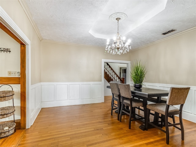 dining space with a textured ceiling, visible vents, a wainscoted wall, light wood finished floors, and an inviting chandelier