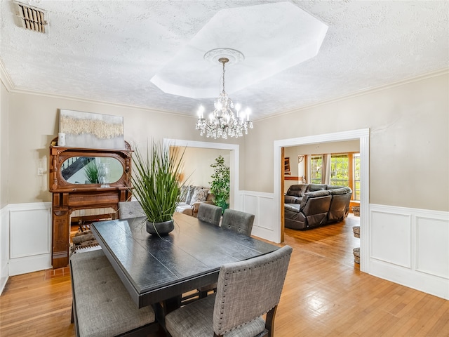 dining room with a textured ceiling, visible vents, a wainscoted wall, an inviting chandelier, and light wood-style flooring