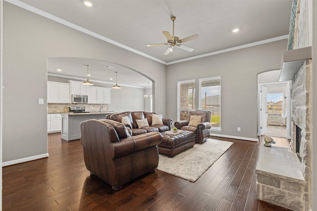 living area featuring ornamental molding, arched walkways, a ceiling fan, and dark wood-type flooring