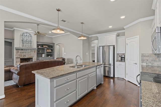 kitchen with a sink, visible vents, stainless steel appliances, arched walkways, and a stone fireplace