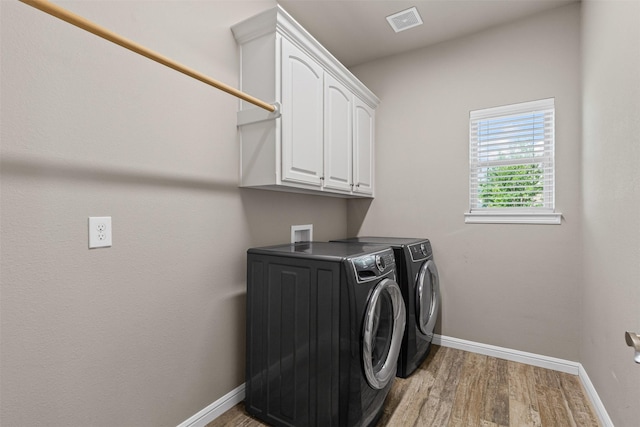 laundry area with independent washer and dryer, light wood-style flooring, visible vents, baseboards, and cabinet space