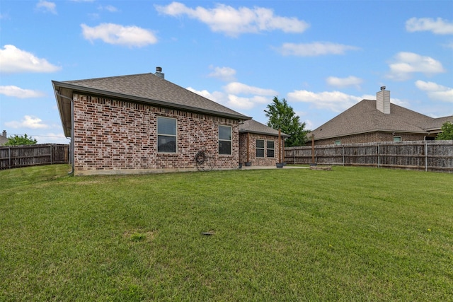 rear view of house featuring brick siding, a fenced backyard, a shingled roof, and a yard
