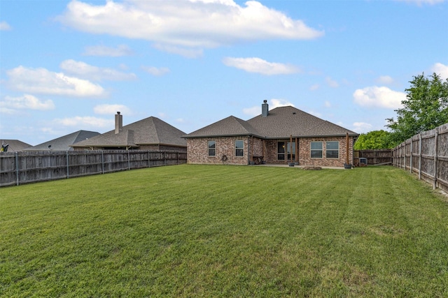 rear view of property featuring a yard, a chimney, a fenced backyard, and brick siding