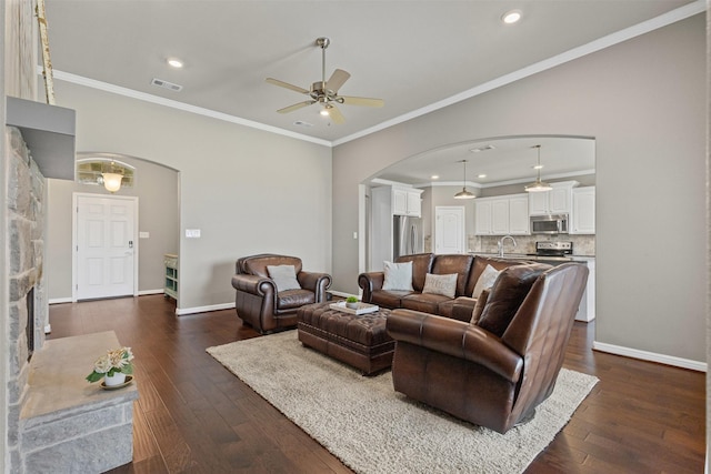 living room with dark wood-type flooring, visible vents, a ceiling fan, and arched walkways