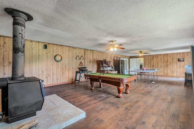 recreation room with billiards, a ceiling fan, a wood stove, wood walls, and wood finished floors