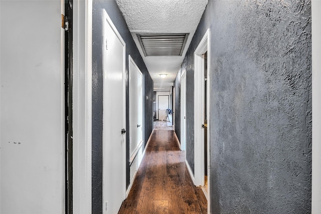 hallway featuring visible vents, a textured ceiling, and wood finished floors