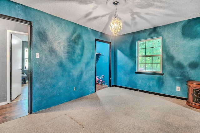 spare room with carpet floors, a textured ceiling, and an inviting chandelier