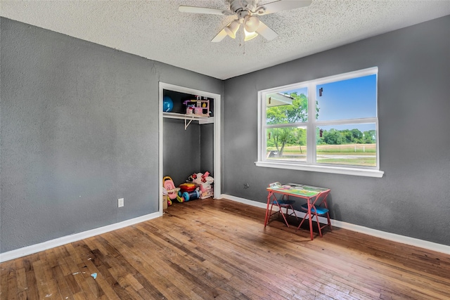 recreation room featuring baseboards, a ceiling fan, a textured wall, and hardwood / wood-style flooring