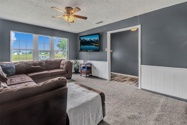 carpeted living room with visible vents, a textured ceiling, ceiling fan, and a wainscoted wall