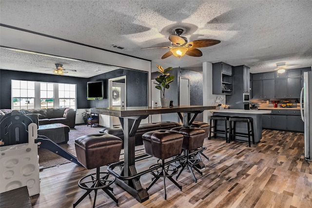 dining room with wood finished floors, a ceiling fan, a textured ceiling, and visible vents