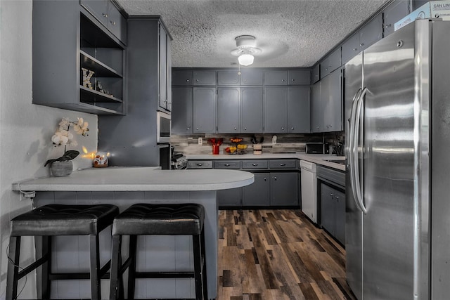kitchen with dark wood finished floors, dishwasher, gray cabinetry, freestanding refrigerator, and a peninsula