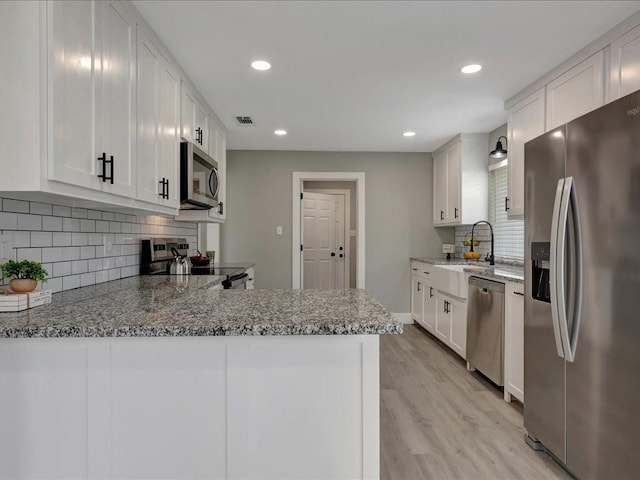 kitchen featuring light stone countertops, light wood-style flooring, appliances with stainless steel finishes, a sink, and visible vents