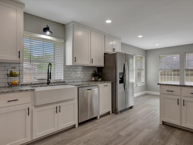 kitchen featuring tasteful backsplash, a sink, appliances with stainless steel finishes, light wood-style floors, and baseboards