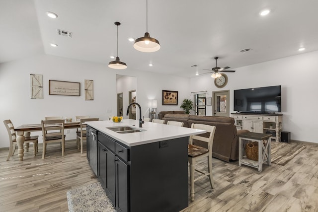 kitchen with a sink, dark cabinetry, light wood-type flooring, a ceiling fan, and visible vents