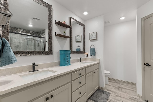 bathroom featuring toilet, double vanity, a sink, and a shower stall