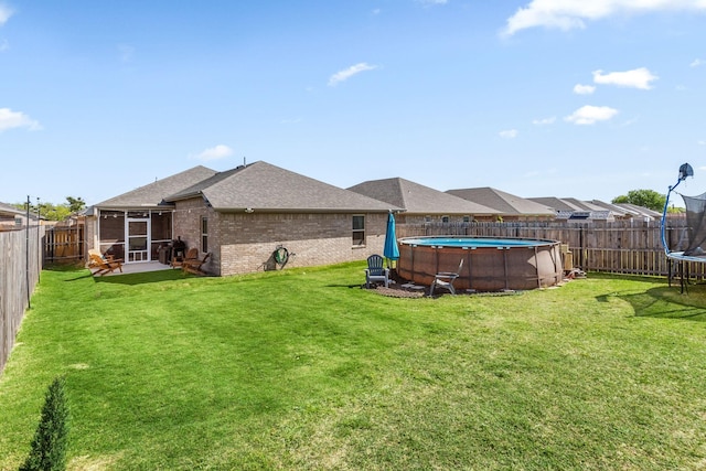rear view of house with a trampoline, a fenced backyard, brick siding, a fenced in pool, and roof with shingles