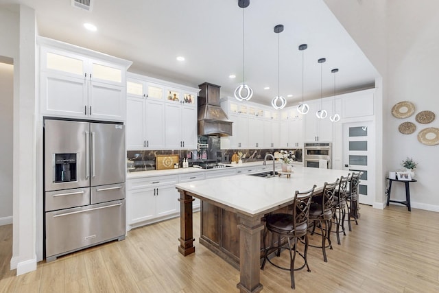 kitchen featuring appliances with stainless steel finishes, custom exhaust hood, light wood-style flooring, and tasteful backsplash