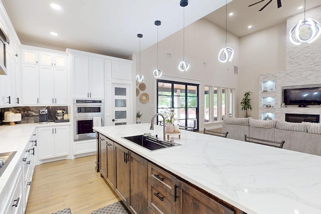 kitchen featuring a sink, white cabinets, double oven, light wood finished floors, and open floor plan