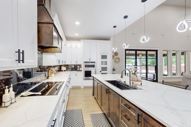 kitchen featuring stainless steel double oven, black electric cooktop, a sink, light stone counters, and white cabinetry