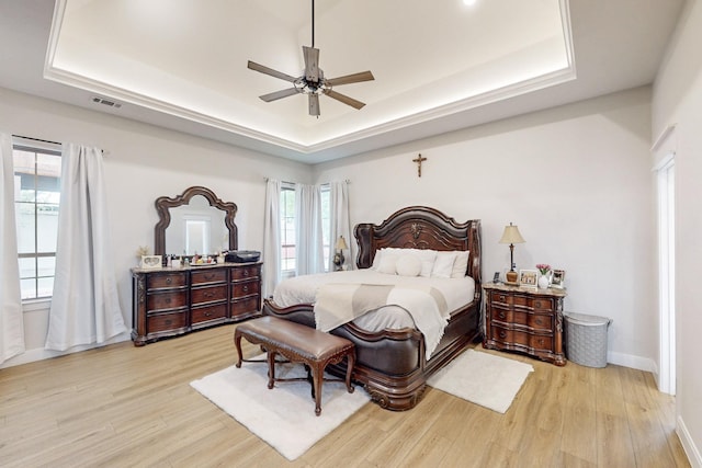 bedroom featuring a raised ceiling, baseboards, light wood-style flooring, and visible vents