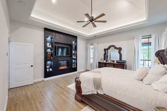 bedroom featuring a fireplace, baseboards, ceiling fan, a raised ceiling, and light wood finished floors