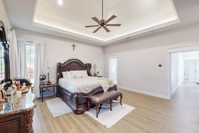 bedroom with baseboards, light wood finished floors, a tray ceiling, and visible vents