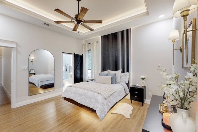 bedroom with baseboards, visible vents, light wood-style flooring, and a raised ceiling
