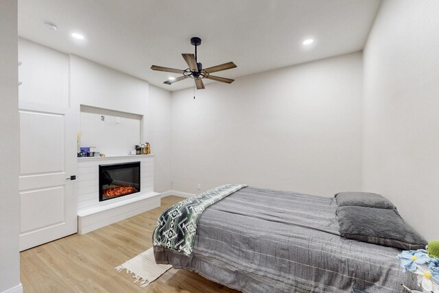 bedroom with ceiling fan, a glass covered fireplace, recessed lighting, baseboards, and wood finished floors